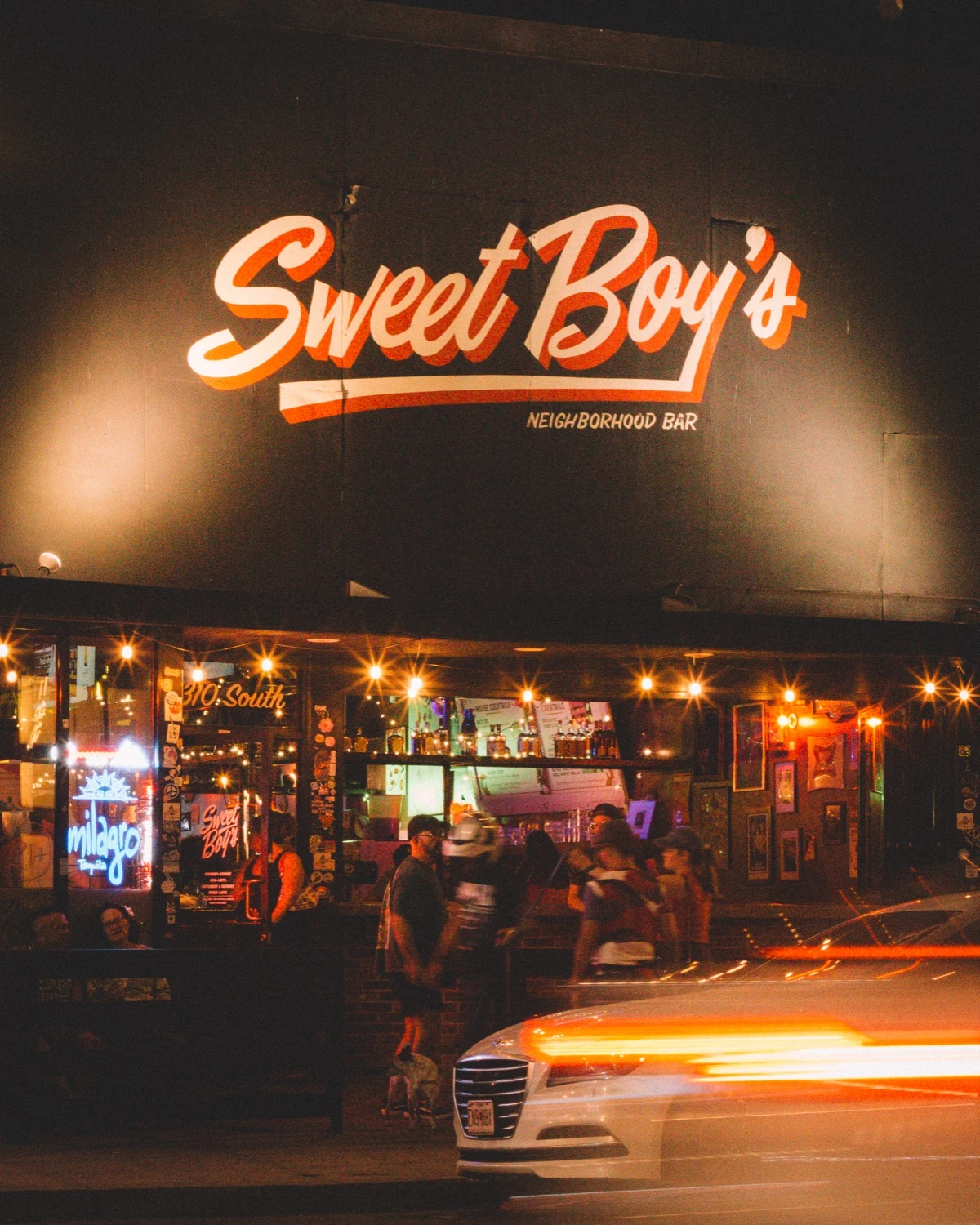 Sweet Boy's at night, with warm string lights across the front of the bar.